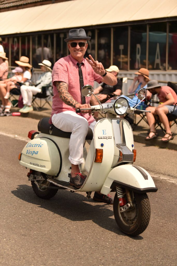 A Vespa driver waves at the crowd.