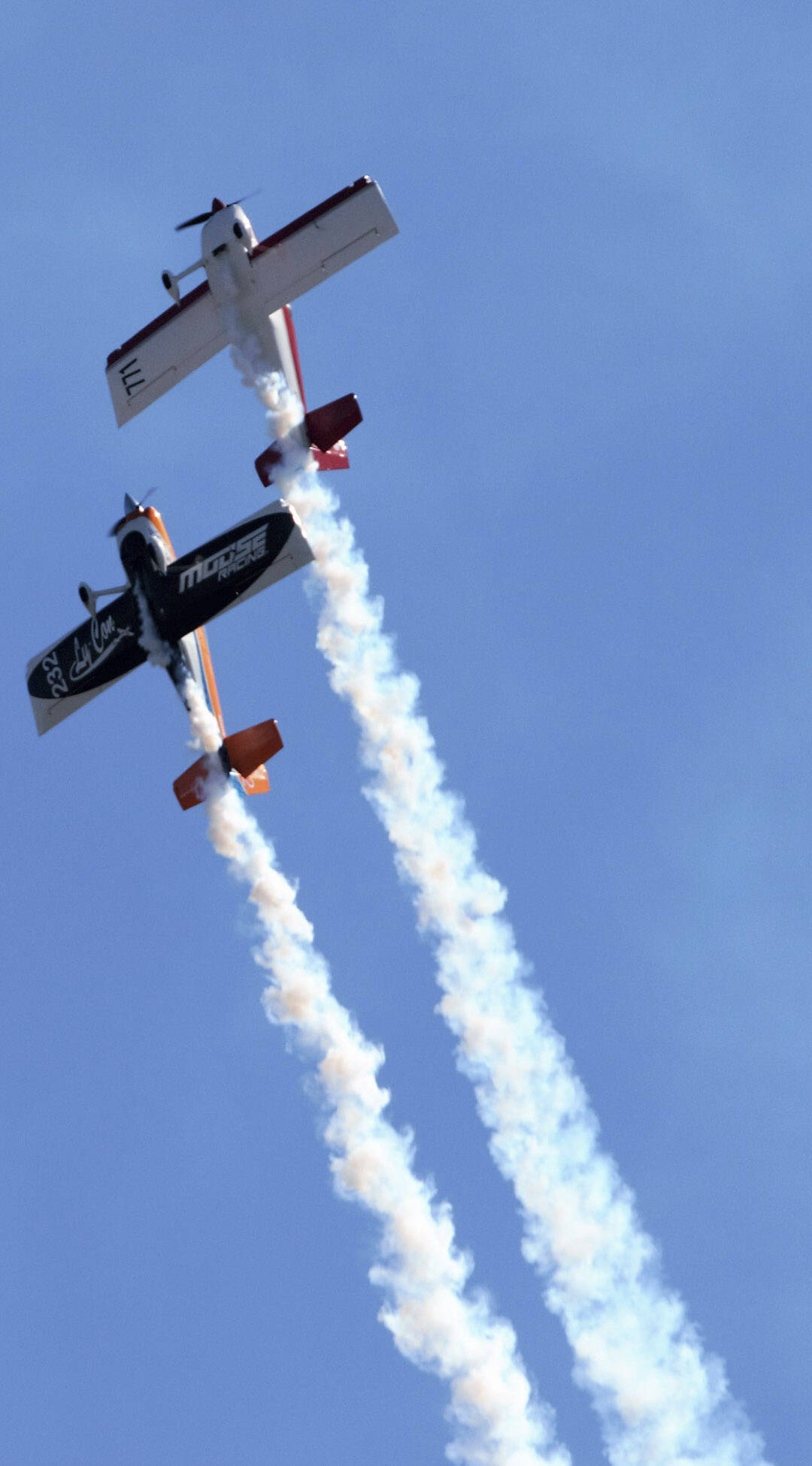 A pair of trick planes ascend into the sky.