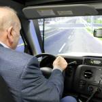 An over-the-shoulder picture gives the vantage point of what the driver sees inside the bus simulator, including a clear daylit roadway.