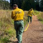 Bainbridge Fire Department staff arrange a hose along a trail through the meadow, which will function as a natural firebreak.