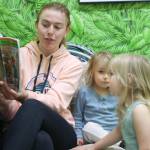 Assistant teacher Taylor Crandell reads a book to two students.